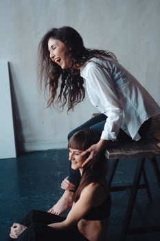 two girls are posing for the camera, one sitting on a chair, other on the floor photo
