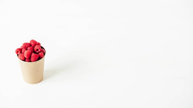 Fresh red raspberries in a paper cup on a white table background photo