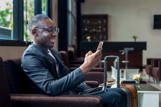 African American businessman is using mobile phone for video call while waiting in airline business departure lounge waiting for boarding the airplane photo