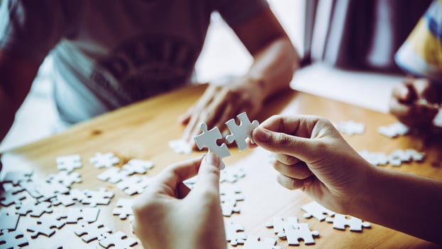 Hands of a person little child and parent playing jigsaw puzzle piece game together on wooden table at home, concept for leisure with family, play with children's development, education and fun. photo