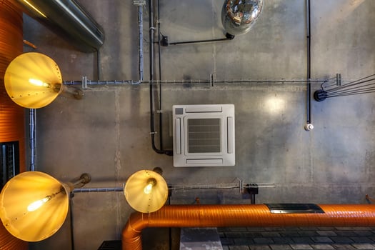 looking up on gray concrete ceiling with halogen spots and edison lamps in loft office room with air conditioning and orange ventilation pipe photo