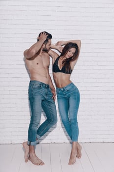 Totally in love. Full length of beautiful young couple looking away while standing against brick wall photo
