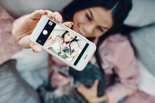 Top view of beautiful young woman in pajamas embracing domestic cat and taking selfie while resting in bed at home photo