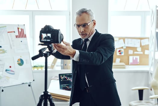 Senior man in elegant business suit adjusting video camera while making social media video photo