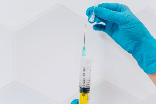 Hands in rubber gloves hold a disposable medical syringe with the drug photo