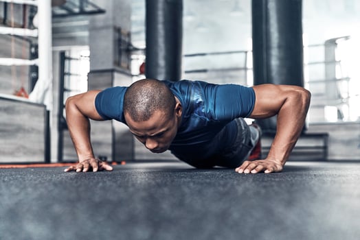 Pushing hard. Handsome young African man in sport clothing doing push-ups while exercising in the gym photo