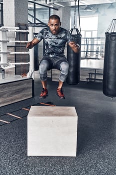 Never give up. Handsome young African man in sport clothing jumping while exercising in the gym photo
