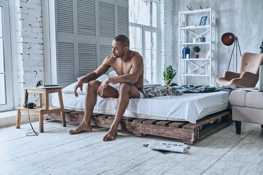 Just one more minute in bed. Sleepy young African man trying to wake up while sitting on the bed at home photo