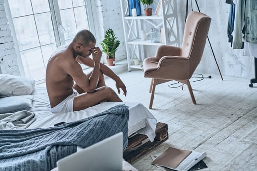 Hard to wake up. Sleepy young African man massaging nose while sitting on the bed at home photo