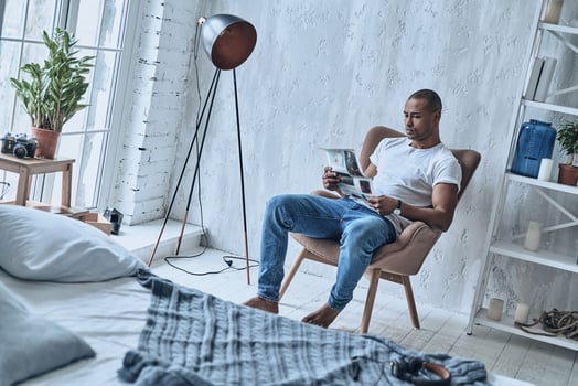 What is new in the world Handsome young African man reading newspaper while sitting in the armchair at home photo