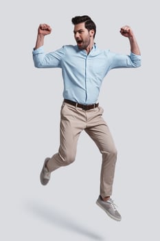 I did it  Full length of handsome young man gesturing and shouting while jumping grey background photo