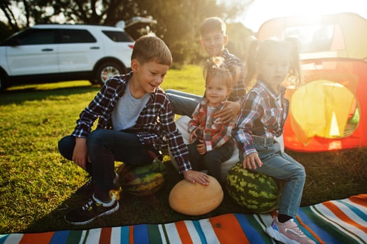 Four kids spending time together. Outdoor picnic blanket, sitting with watermelons. photo
