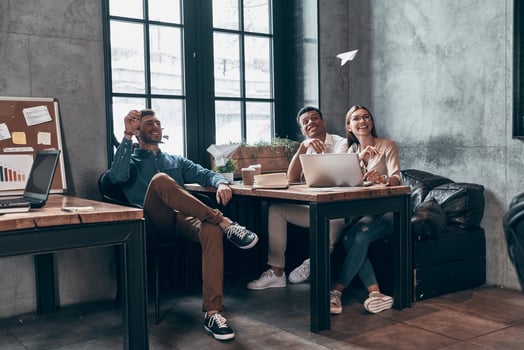Group of young playful coworkers in smart casual wear smiling and throwing paper airplane photo