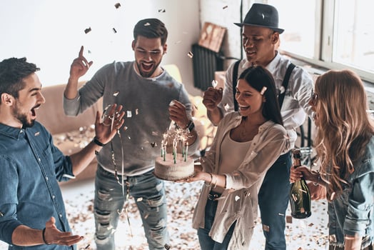 Time for a birthday cake. Top view of happy young man celebrating birthday among friends while standing in room with confetti flying around photo