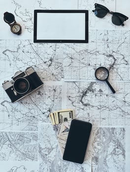 Just travel. High angle shot of sunglasses, photo camera, compass, magnifying glass, smart phone, passport and currency lying on map
