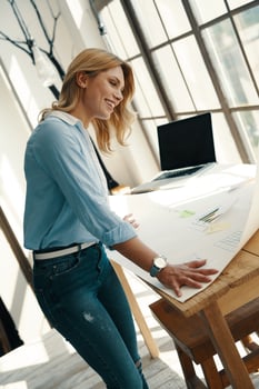 Busy young woman making a graph on the blueprint and smiling while working in the office photo