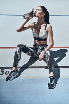 Time to rest. Top view of young woman in sports clothing drinking water while sitting on the running track outdoors photo