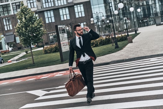 Confident businessman. Full length of young man in full suit crossing the street while walking outdoors photo