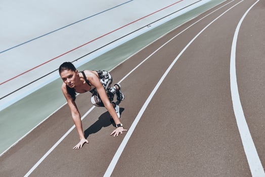 Pushing herself to the limit. Top view of young woman in sports clothing standing on the start line while running outdoors photo