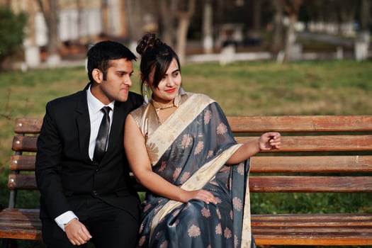 Elegant and fashionable indian friends couple of woman in saree and man in suit sitting on bench. photo