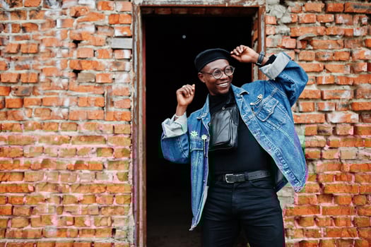 African american man in jeans jacket, beret and eyeglasses against brick wall at abandoned roof. photo