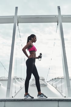 Tired after training. Full length of modern young woman in sports clothing drinking water while standing outdoors photo