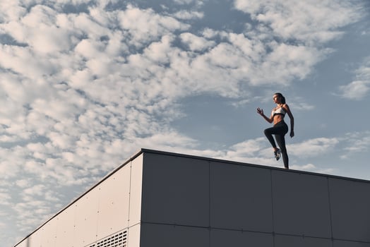 Power and beauty. Full length of modern young woman in sports clothing jumping while exercising time on the roof outdoors photo