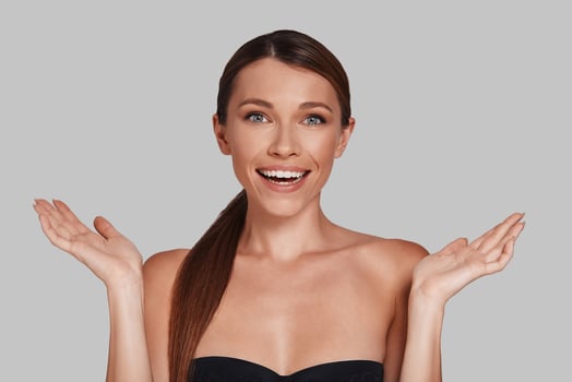 Beautiful woman. Attractive young woman looking at camera and gesturing while standing against grey background photo