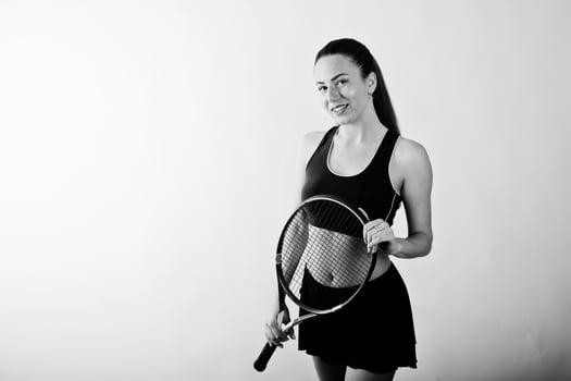 Black and white portrait of beautiful young woman player in sports clothes holding tennis racket while standing against white background. photo