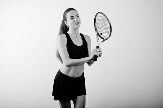 Black and white portrait of beautiful young woman player in sports clothes holding tennis racket while standing against white background. photo
