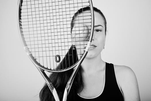 Black and white portrait of beautiful young woman player in sports clothes holding tennis racket while standing against white background. photo
