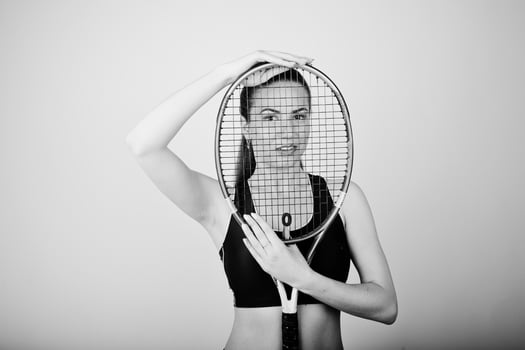 Black and white portrait of beautiful young woman player in sports clothes holding tennis racket while standing against white background. photo