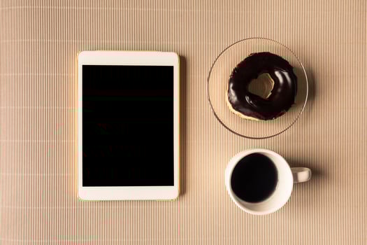 Top view of tablet with coffee cup and donut on table. photo