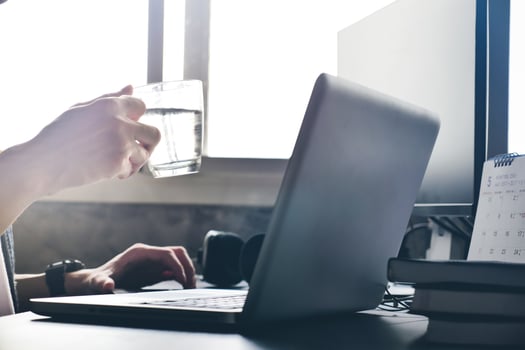 Casual man holding a cup of water and using computer on the desk. photo