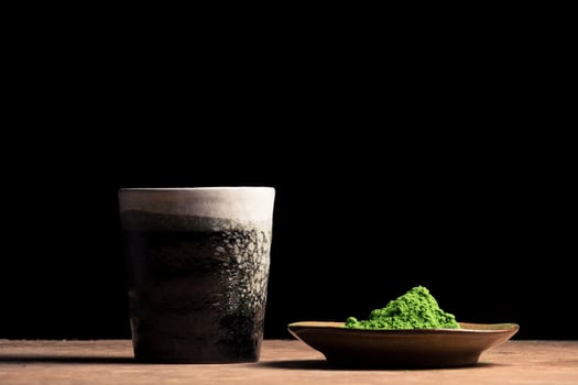 a ceramic cup and green tea powder on the table, black background. Free space for text photo