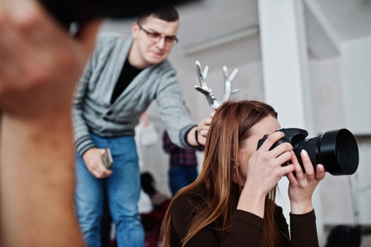 The team of two photographers shooting on studio. Professional photographer on work. One of them joking and holds horns over head. photo