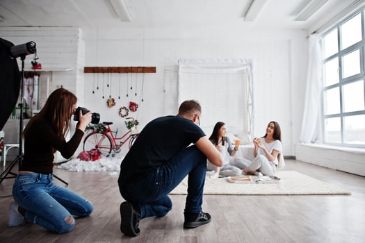 The team of two photographers shooting on studio twins girls who are eating pizza. Professional photographer on work. photo