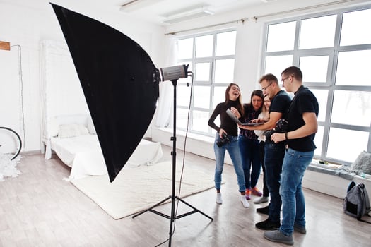Photographer explaining about the shot to his team in the studio and looking on laptop. Talking to his assistants holding a camera during a photo shoot. Teamwork and brainstorm.