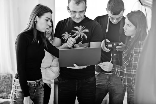 Photographer explaining about the shot to his team in the studio and looking on laptop. Talking to his assistants holding a camera during a photo shoot. Teamwork and brainstorm.