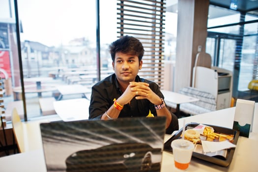 Stylish indian man sitting at fast food cafe against his laptop. photo
