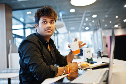 Stylish indian man sitting at fast food cafe against his laptop and drink soda. photo