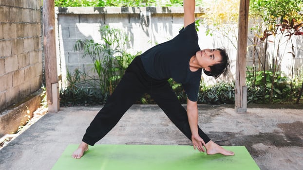 Healthy living concept of young Asian man practicing yoga asana Triangle Pose, working out,  poses on a green yoga mat. outside exercise in the garden. healthy lifestyle. photo