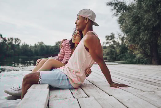 Joy of being in love. Happy young couple embracing and smiling while sitting on the pier near the lake photo