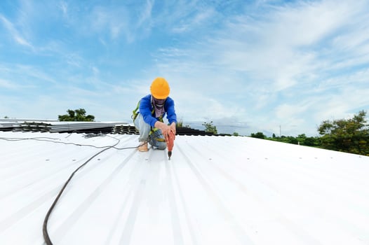 Construction worker in work clothes installing new roofing tools roofing tools, electric drill, and use on new wooden roofs with metal sheets. photo