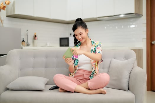 Smiling young asian woman using mobile phone app playing game, relax on sofa. photo