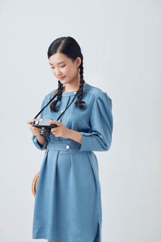 Smiling good looking Asian woman with long pigtail holds retro camera, takes pictures during her awesome trip photo