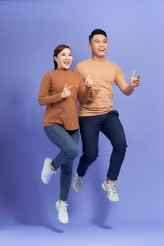 Excited young Asian couple man and woman jumping and pointing with happy and fun over purple background photo