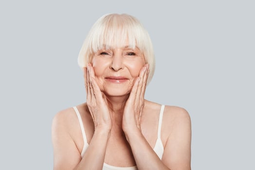 Taking good care of her skin. Beautiful senior woman looking at camera and smiling while standing against grey background photo