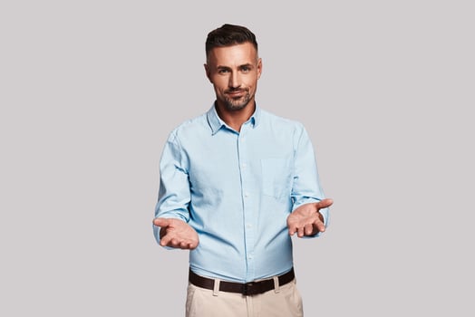 Welcome Good looking young man keeping arms outstretched and looking at camera while standing against grey background photo