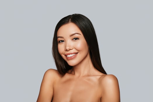 Shiny beauty. Beautiful young Asian woman looking at camera and smiling while standing against grey background photo